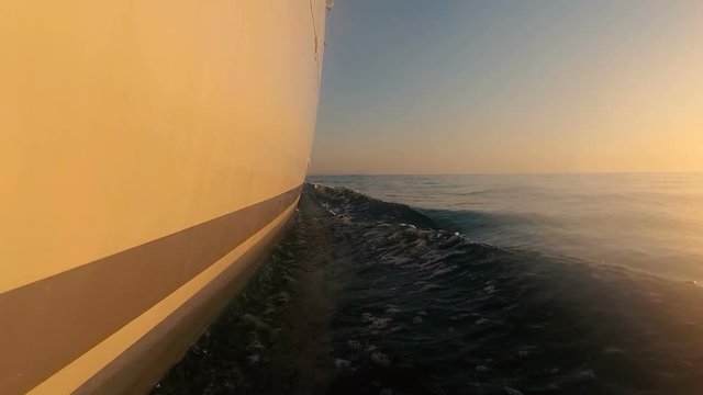 the boat sails on the waves at sunset. Low shot close to water from starboard side