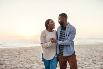 Young African couple walking on a beach at sunset laughing