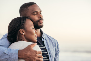 Content African couple standing on a beach hugging each other