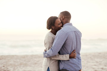 Happy young African couple embracing on a beach at dusk