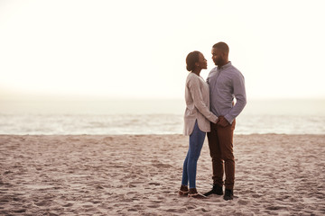 Content young African couple standing on a beach at dusk