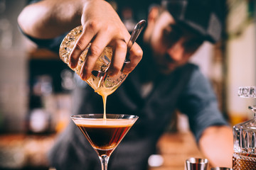 close up of barman hand pouring alcoholic cocktail in martini glass