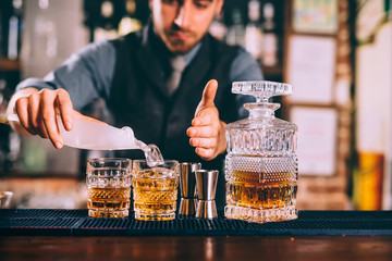 Portrait of bartender adding ice to delicious alcoholic whisekey cocktails