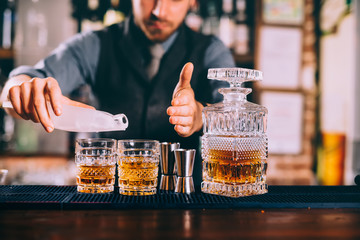 Close up of barman hands adding ice and whiskey to modern urban cocktails. Sky bar serving elegant...