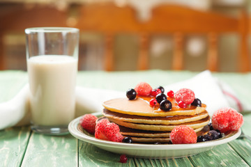 Stack of pancakes with frozen berries poured with honey on wooden kitchen table. Selective focus.