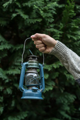 Fototapeta na wymiar Old lantern held in a hand in front of a dark green tree