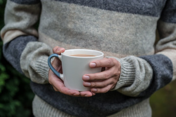 Hands holding a cup of warm coffee in a forest