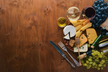 A bottle of wine, and a large assortment of cheeses, honey, nuts and spices, on a wooden table. Top view. Free space for text.