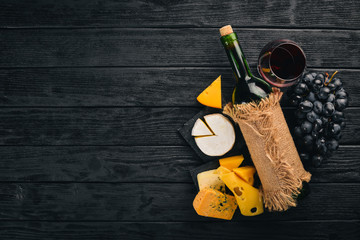 A bottle of wine, grapes and cheese on a wooden background. Cheese brie, blue cheese, gorgonzola, fuete, salami. Italian Traditional Cuisine. Free space for text. Top view.