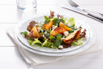 Fresh mixed salad on white. Lettuce and arugula leaves with grilled peach and blue cheese.