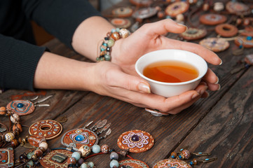 Hands with a tea bowl on a wooden table with clay ethnic decorations. View from above
