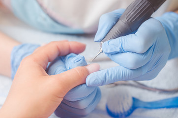 Master of manicure in rubber gloves makes a manicure with the help of a nail polish machine on the nails of a woman