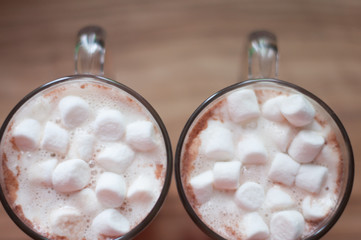 Fototapeta na wymiar Two glass cups of latte or cacao from above with marshmallows, cinnamon and milk foam standing on wooden table