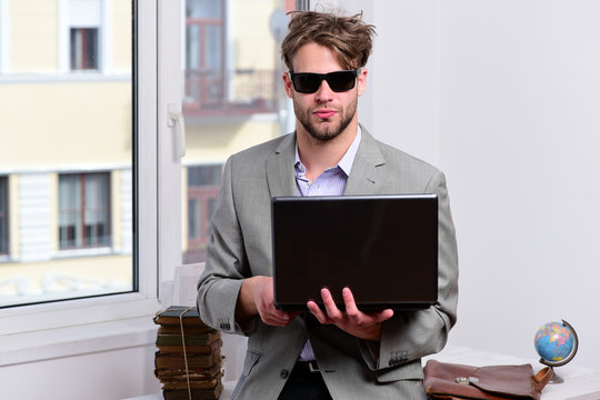 Businessman with laptop and pile of books on window background