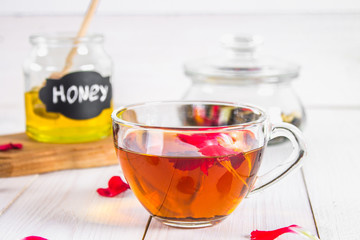 Floral black tea, honey can, petals on a white wooden table.