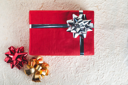 Top view on red present with silver ribbon and bow on textured paper background