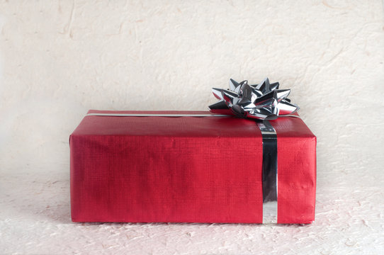 One red gift box or present with silver ribbon and bow on textured paper surface for Christmas design