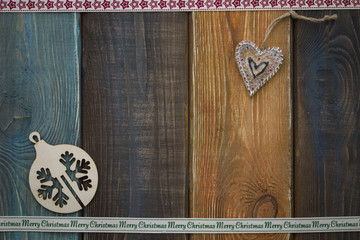 A colored wooden Christmas background with wooden Christmas-tree ball and gingerbread. A star patterned ribbon at the top. A Merry Cristmas inscription ribbon on the bottom. Copy space. Top view