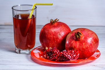 glass beaker with pomegranate juice and pomegranate fruits on a light wooden background