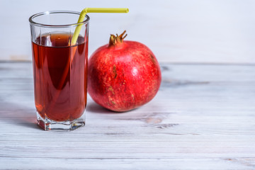 glass beaker with pomegranate juice and pomegranate fruits on a light wooden background