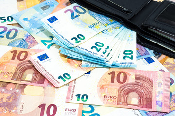 Pile of various kinds euro banknotes on desk with many tweny euro bills in  black leather wallet.