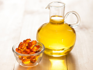 Fish oil in a jug and capsules on wooden texture and table