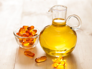 Fish oil in a jug and capsules on wooden texture and table