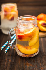 Mason jar glass of homemade peach iced water on a rustic wooden background.