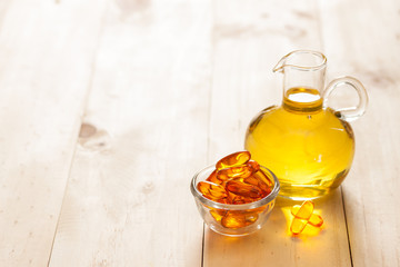 Fish oil in a jug and capsules on wooden texture and table
