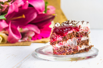 A piece of cake and a bouquet of flowers on a white wooden table. Celebrating the birthday, a gift.