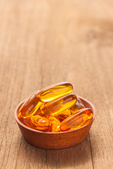 A bowl of Fish oil capsules on wooden texture, vertical view