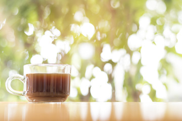 black Coffee in the glass cup on wood floor and  background is bokeh. Bright green with Morning atmosphere.
