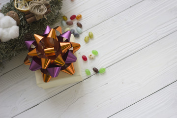 A beige gift box with a bright metalic bow, pine twigs on a light wooden background Close up. Copy space. Top view