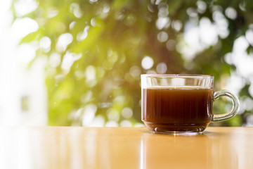 black Coffee in the glass cup on wood floor and  background is bokeh. Bright green with Morning atmosphere.