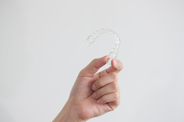 Hand holding clear invisalign braces on white background, new technology of dental equipment