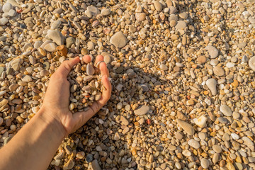 Female hand touches little pebbles on a sea beach