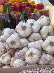 pile of garlic heads of Vessalico exposed at a banquet of the market. In the background wine bottles and yellow and red peppers in the exhibition.