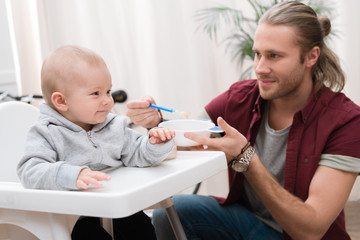 Obraz na płótnie Canvas father feeding his cheerful son with baby food at home