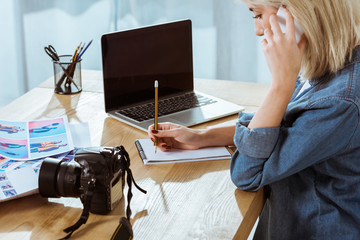 side view of photographer talking on smartphone while working at workplace with laptop in studio