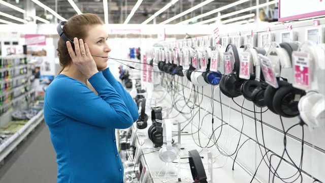 Happy woman is testing headphones in modern store.