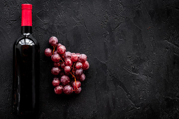 Bottle of red wine near bunch of grapes on black background top view copyspace