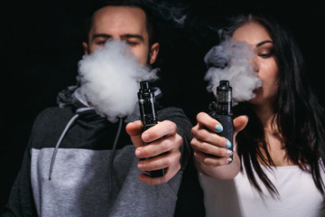 Couple vaping e-cigarette with smoke on black