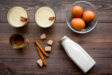 Make eggnog classic recipe. Eggs, milk, cinnamon, whiskey on dark wooden background top view