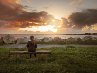 Girl sitting on a wooden bench and watching sunset over Galway, West coast of Ireland, Atlantic ocean.