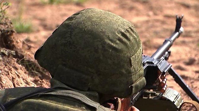 A machine gunner in a helmet and camouflage takes aim and fires a machine gun, the machine gunner conducts targeted fire from cover.