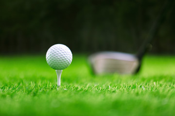 Golf ball on tee with golf club on green grass