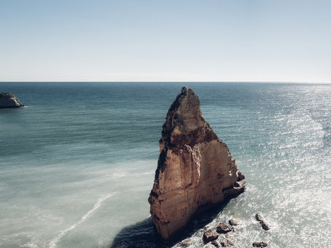 Big rock sitting in the blue ocean on a sunny day