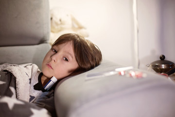 Sick child boy lying on the sofa with a fever