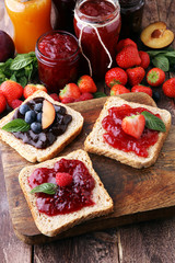 Sandwiches with plum, strawberry jam and fresh fruits on wooden background