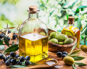 Olive oil and berries are on the wooden table under the olive tree.